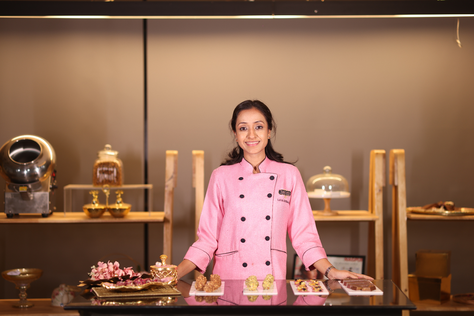 Lulua Kapadia in her chocolate studio, in chef whites behind a display of handcrafted chocolates